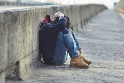 Kind zit voorover gebogen met handen op zijn hoofd, op een brug tegen een betonnen rand geleund.